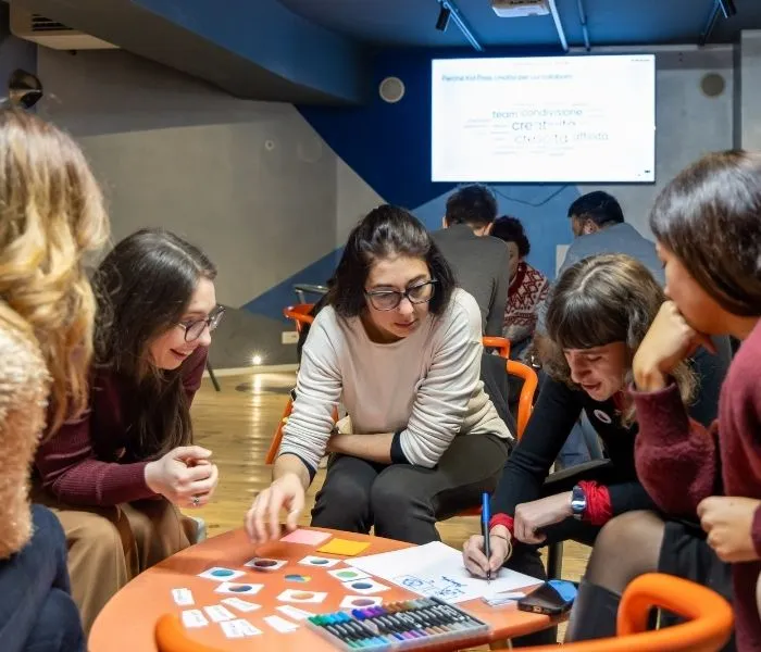 Il team Kid Pass lavora in piccoli gruppi attorno a un tavolo, con cartoncini e pennarelli